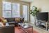 Bright and inviting living room with modern leather sofa, stylish coffee table, and large TV, complemented by a lush indoor plant and chic wall clock.