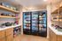 Modern and inviting pantry with sleek wooden cabinets, well-stocked shelves, and glass-door fridges filled with a variety of snacks and beverages.