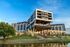 Modern architectural marvel with sleek design and elevated structure, surrounded by lush greenery and a serene waterfront backdrop.