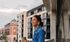 Woman enjoying city view from a modern apartment balcony, surrounded by stylish architecture and vibrant urban atmosphere.