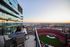 Breathtaking cityscape view from a modern high-rise balcony overlooking a sports stadium, featuring a cozy seating area perfect for enjoying beautiful sunsets.