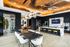 Luxurious modern kitchen and dining area with sleek marble countertops, stylish island with vibrant yellow stools, striking chandelier, and sophisticated wine rack display.