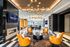 Elegant lobby of luxury apartment with modern decor, vibrant orange chairs, chic lighting, fireplace, and city view backdrop.