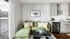 Bright, modern living area featuring a green velvet sofa, decorative cushions, and a compact kitchen with stainless steel appliances.