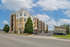 Modern urban apartment building with stylish balconies and ample parking, set against a vibrant blue sky.