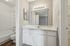 Modern bathroom featuring a sleek vanity, large mirror with elegant lighting, and a pristine bathtub with chic white fixtures at Driscoll Place.