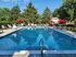 Hidden Creek Apartments Pool | Inviting outdoor pool area surrounded by lush greenery, featuring comfortable lounge chairs and vibrant red umbrellas for relaxation.