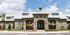 Charming residential building with elegant stone facade and inviting entrance, adorned with colorful balloons, surrounded by lush landscaping under a vibrant blue sky.