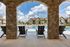 Inviting view of a luxurious apartment community pool framed by elegant stone arches, featuring comfortable lounge chairs under a bright blue sky.