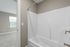 Bright and modern bathroom with elegant white bathtub and sleek fixtures, featuring a cozy adjoining carpeted bedroom with a large window.