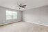 Bright, spacious bedroom with a modern ceiling fan and plush carpeting, featuring a large window with blinds for natural light.
