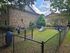 Inviting pet-friendly area with agility equipment and seating, surrounded by lush greenery and charming brick buildings.
