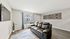 Bright living room with modern decor featuring a sleek black leather sofa, stylish wall art, and a large window with elegant teal curtains.