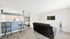 Bright open-concept living area featuring a modern kitchen with a breakfast bar, stylish seating, TV, and cozy bedroom corner.