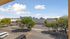 Stunning city skyline view from an apartment balcony with lush green trees and a clear blue sky.