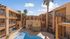 Sunlit apartment complex with a central pool and palm trees, featuring modern three-story layout.