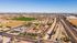 Captivating aerial view of a sprawling residential community with lush landscapes beside a bustling highway, showcasing proximity to amenities and expansive green fields.