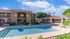 Charming apartment complex with a sparkling swimming pool, sunny courtyard, and lush greenery, perfect for relaxation.