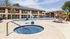 Charming apartment complex featuring a sunlit pool area with a relaxing hot tub, surrounded by lush palm trees and stylish lounge chairs for a perfect outdoor escape.
