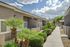 Charming apartment exterior with a lush pathway, vibrant greenery, and clear blue skies creating a welcoming ambiance.