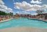 Inviting outdoor pool area with elegant lounge chairs, surrounded by lush greenery under a brilliant blue sky.