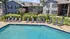 Inviting apartment complex featuring a refreshing swimming pool surrounded by modern lounge chairs, lush greenery, and charming two-story residential buildings.
