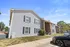Charming two-story apartment building with modern gray siding, stylish black shutters, and welcoming brick accents. Green lawn and convenient parking highlight the inviting entrance.