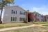Charming two-story apartment building with brick and siding exterior, featuring black shutters and well-maintained landscaping under a clear blue sky.