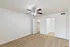 Bright and spacious bedroom with elegant wooden flooring, featuring a stylish ceiling fan and ample closet space. Modern en-suite bathroom visible through open double doors.