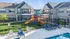 Inviting apartment complex with modern exteriors, featuring a colorful playground and a refreshing pool area with lounge chairs.