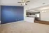 Inviting open-concept living space with plush beige carpet, a stylish blue accent wall, and a modern kitchen with stainless steel appliances and dark wood cabinetry.