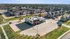 Inviting neighborhood with modern apartment complex and commercial building surrounded by lush greenery and broad streets under a clear blue sky.