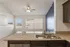 Bright and airy kitchen with granite countertops, modern sink, and open living area featuring large windows and ceiling fan.