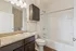 Modern bathroom featuring elegant granite countertop, dark wood cabinetry, and a sleek white bathtub with chrome fixtures.