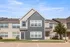 Charming suburban townhouse with modern grey and beige facade, large windows, and manicured lawns beneath a clear blue sky.