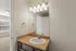 Bright and elegant bathroom with a granite countertop and modern light fixture, offering a glimpse of spacious adjacent room through an open doorway.