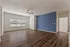 Spacious living room with elegant wooden flooring, a deep blue accent wall, and ample natural light from large windows.