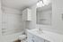 Pristine modern bathroom featuring sleek white cabinetry, elegant fixtures, and a spacious mirror, perfect for a contemporary living space.