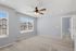 Bright, spacious room with large windows, stylish ceiling fan, and plush carpet, perfect for a cozy living area.