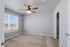 Bright and airy bedroom with fresh carpet, modern ceiling fan, and expansive window with scenic views.