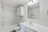 Modern bathroom featuring a sleek white vanity, spacious mirror, and pristine bathtub, offering a bright and inviting space.