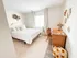 Inviting bedroom with a cozy atmosphere, featuring a plush bed, elegant wicker desk, and charming decor. Natural light streams through a large window, enhancing the serene ambiance.