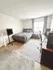 Bright bedroom with large window, cozy grey bedspread, sleek wooden floors, and versatile working desk, creating a serene and inviting space.