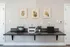 Modern home office setup with sleek black countertop, two laptops, a printer, and minimalistic wall art for a contemporary workspace.
