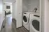 Modern laundry area with sleek washer and dryer units, complemented by elegant wood flooring and a glimpse into a cozy, stylish room.