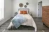 Charming bedroom with modern decor, featuring a cozy bed, stylish wood dresser, and bright natural light from large window.