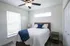 Charming bedroom with modern ceiling fan, cozy wooden bed, and ample natural light from large windows.