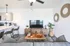 Modern living room with stylish decor, featuring a cozy gray sofa, elegant wood accents, and a sleek TV setup. Open-concept kitchen with chic bar stools and pendant lighting.