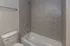 Bright and modern bathroom with elegant tiled shower wall, classic white bathtub, and sleek toilet design.