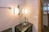 Elegant bathroom featuring a modern glass vessel sink, stylish lighting, and a warm wooden door leading to a cozy hallway.